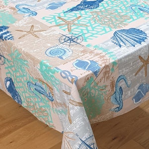 Może przedstawiać: Biały obrus w stylu marynistycznym z motywami koników morskich, gwiazd morskich, muszli, koralowców i kompasów. Obrus ma jasnoniebieski, beżowy i zielony kolor.