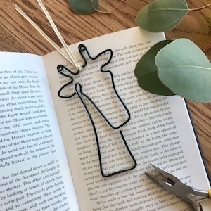May include: A black metal giraffe bookmark with a white ribbon. The bookmark is lying open on a book with text about the Earth and Moon.