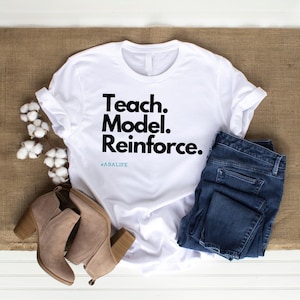 May include: White t-shirt with black text that reads "Teach. Model. Reinforce." and the hashtag #ABALIFE.