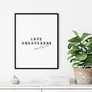 Puede incluir: Una impresión enmarcada en negro con el texto "LOVE AMBASSADOR assigned by God" sobre un fondo blanco.