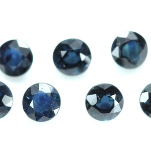 May include: Seven round, faceted, dark blue gemstones on a white background.