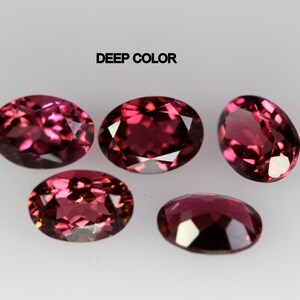 May include: Five oval-shaped gemstones with a deep red color. The gemstones are arranged in a semi-circle on a white surface. The text "DEEP COLOR" is printed above the gemstones.