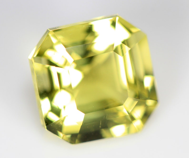 May include: A yellow gemstone with a square cut and a faceted finish.