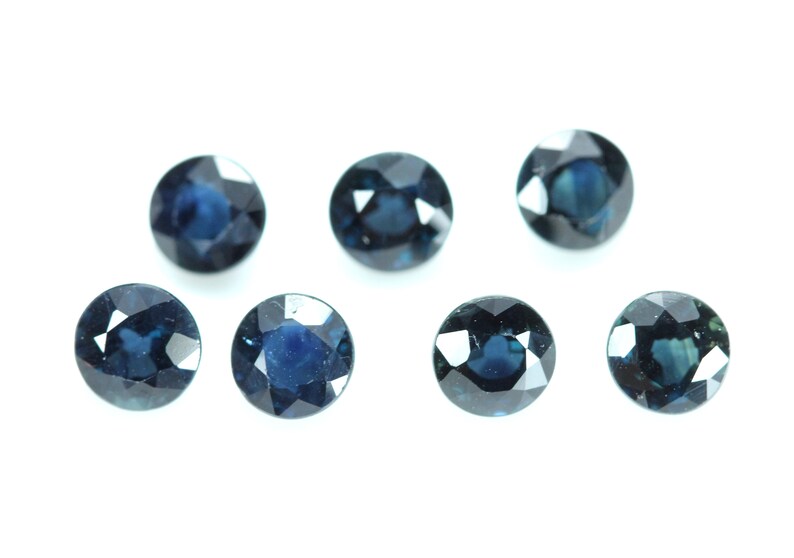 May include: Eight round, faceted, dark blue gemstones. The gemstones are arranged in two rows of four, with the top row slightly offset from the bottom row.