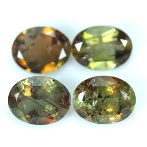 May include: Four oval-shaped gemstones with a green, brown, and gold color. The gemstones are faceted and have a shiny finish.