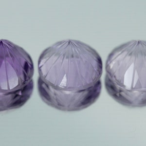 May include: Three faceted amethyst gemstones, each with a pointed top and a round base. The gemstones are a light purple color and have a shiny, polished finish.