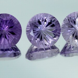 May include: Three round, faceted gemstones with a starburst pattern. The gemstones are purple, clear, and a light purple.