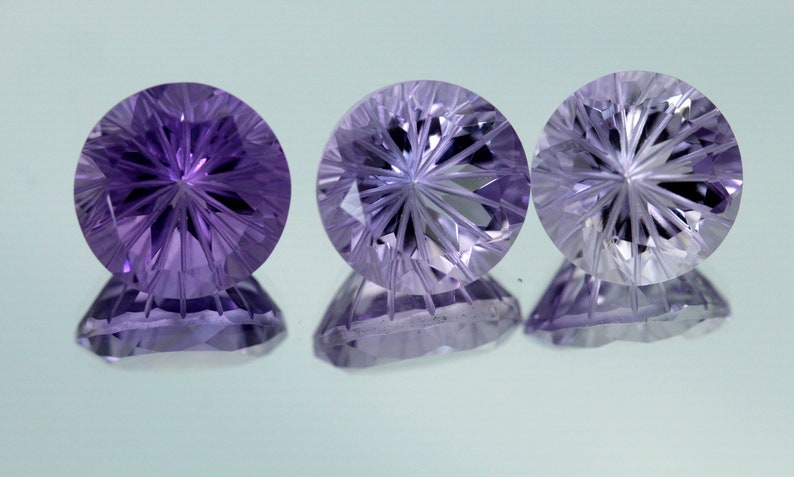 May include: Three round, faceted gemstones with a starburst pattern. The gemstones are purple, clear, and a light purple.