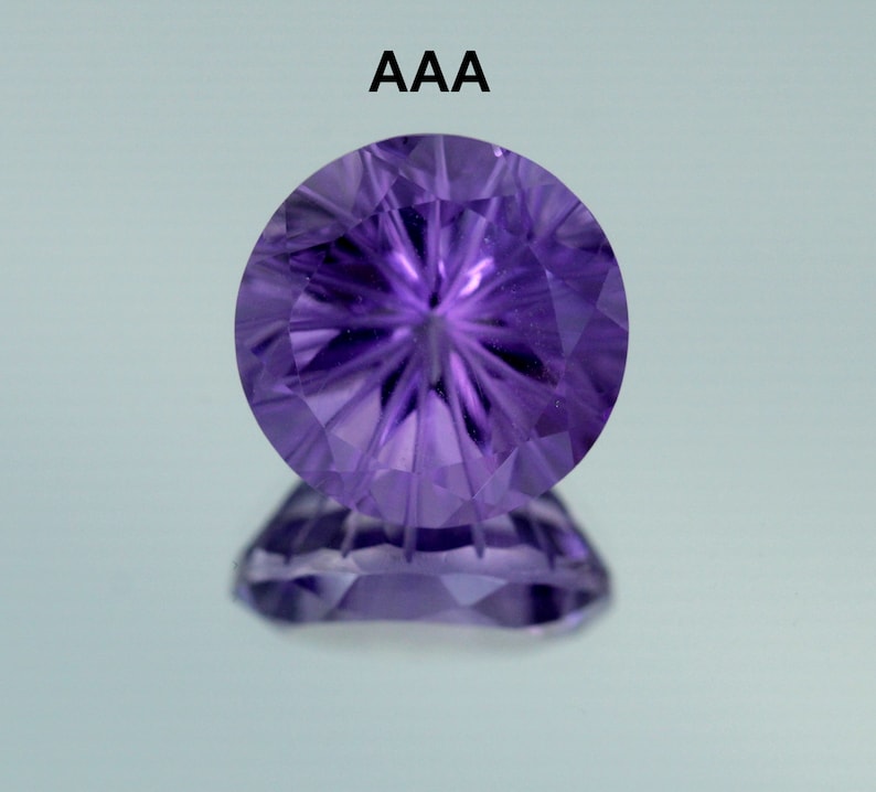 May include: A round, purple amethyst gemstone with a starburst pattern cut into the surface. The gemstone is labeled "AAA" indicating its quality.