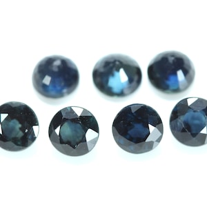 May include: Seven round, faceted, dark blue gemstones. The gemstones are arranged in a semi-circle on a white background.