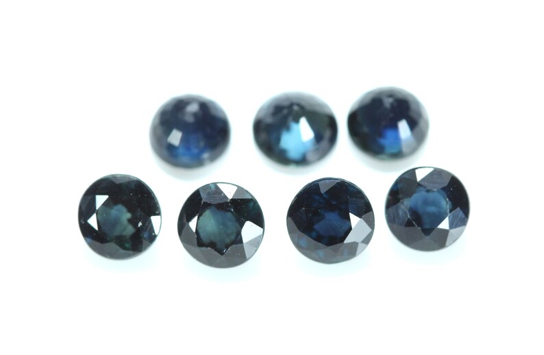 May include: Seven round, faceted, dark blue gemstones. The gemstones are arranged in a semi-circle on a white background.