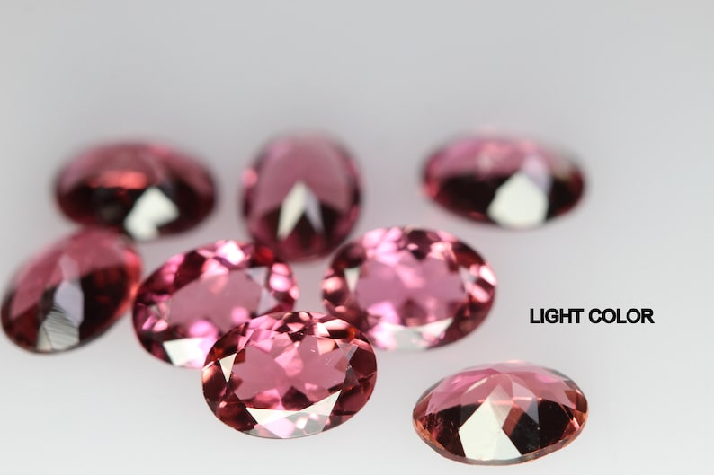 May include: A group of eight oval-shaped, light pink gemstones. The gemstones are faceted and have a high shine.  LIGHT COLOR