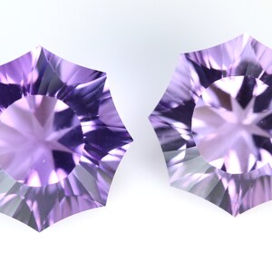 May include: Two faceted, star-shaped gemstones with a light purple hue. The gems have a central circular facet surrounded by a series of triangular facets, creating a starburst effect. The background is plain white.