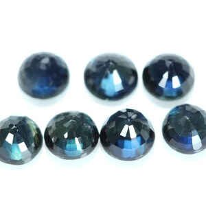 May include: Seven round, faceted, dark blue gemstones on a white background.