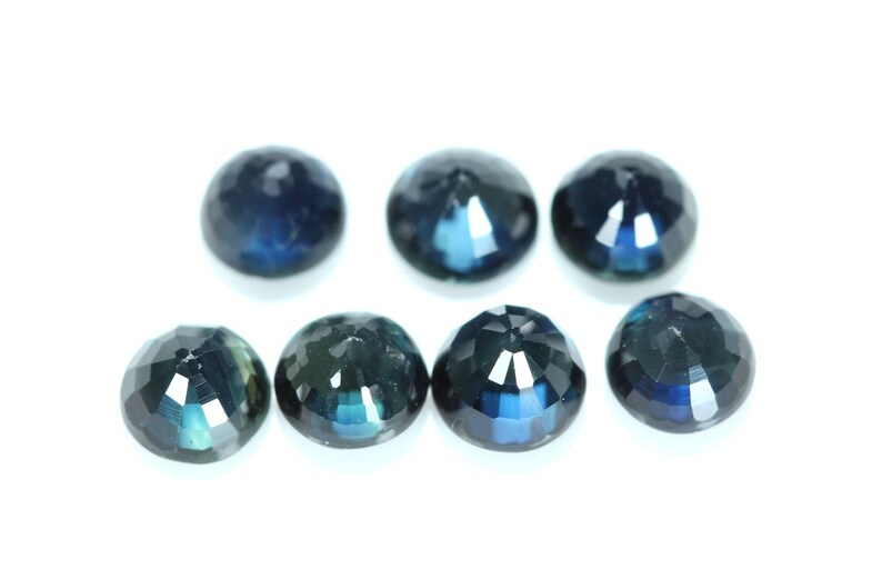 May include: Seven round, faceted, dark blue gemstones on a white background.