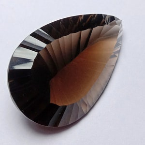 May include: A faceted, teardrop-shaped gemstone with a gradient of brown and smoky gray hues. The gem's surface is cut with precise angles, creating a play of light and shadow. The overall effect is a polished, elegant appearance.