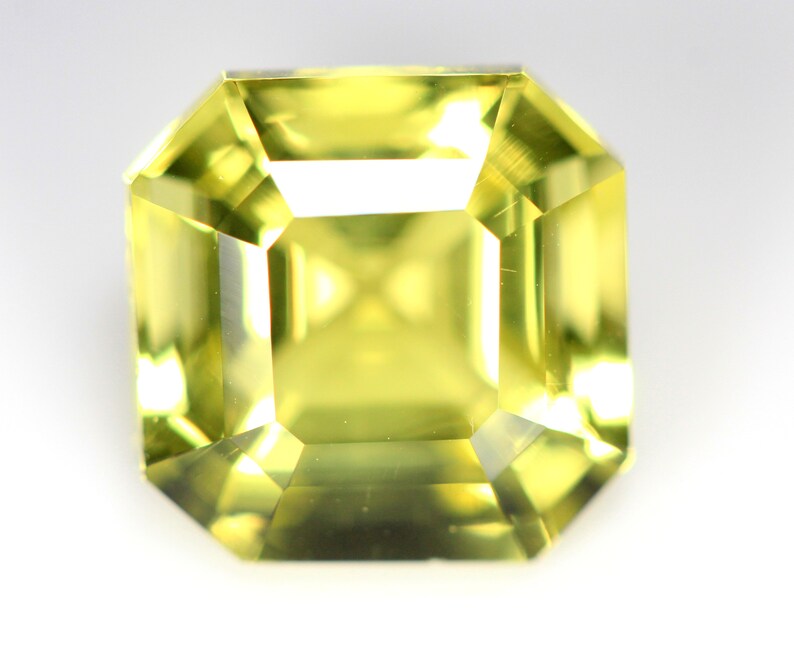May include: A bright yellow gemstone cut into an emerald shape.