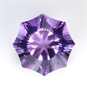 May include: A faceted, starburst-shaped gemstone in shades of purple. The gem has a symmetrical design with pointed edges radiating from a central point. The facets create a play of light and shadow, enhancing its brilliance.