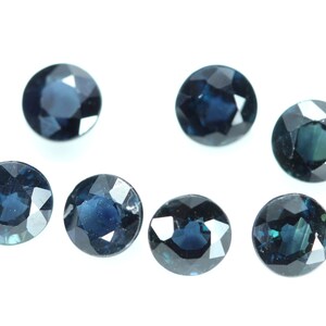 May include: Six round, dark blue gemstones with faceted edges. The gemstones are arranged in a semi-circle on a white background.