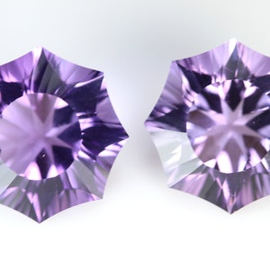 May include: Two faceted, star-shaped gemstones with a light purple hue. The gems have a central circular facet surrounded by radiating facets, creating a starburst effect. The gems are displayed against a white background.