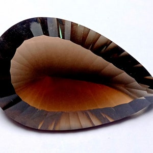 May include: A faceted, pear-shaped gemstone with a gradient of brown hues. The gem has a dark, almost black, border that transitions to a lighter brown center. The cut of the stone creates a play of light and shadow.