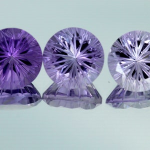 May include: Three round, faceted amethyst gemstones with a starburst pattern in the center. The gemstones are purple and have a clear, glassy appearance.