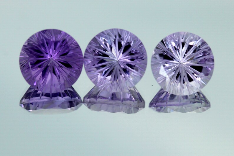 May include: Three round, faceted amethyst gemstones with a starburst pattern in the center. The gemstones are purple and have a clear, glassy appearance.