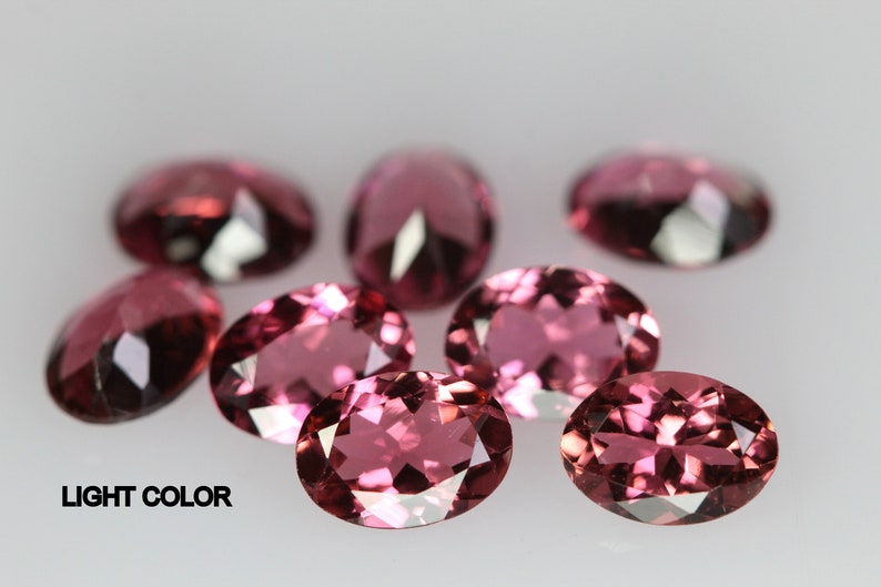 May include: A group of seven oval-shaped, light pink gemstones. The gemstones are faceted and have a shiny, polished finish.