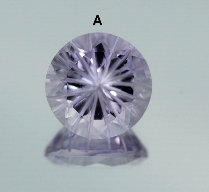 May include: A clear, faceted gemstone with a starburst pattern in the center. The gemstone is a light purple color and has a reflective surface.