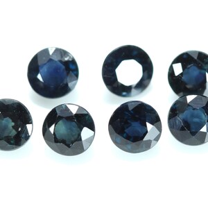 May include: Seven round, faceted, dark blue gemstones. The gemstones are arranged in a semi-circle on a white background.