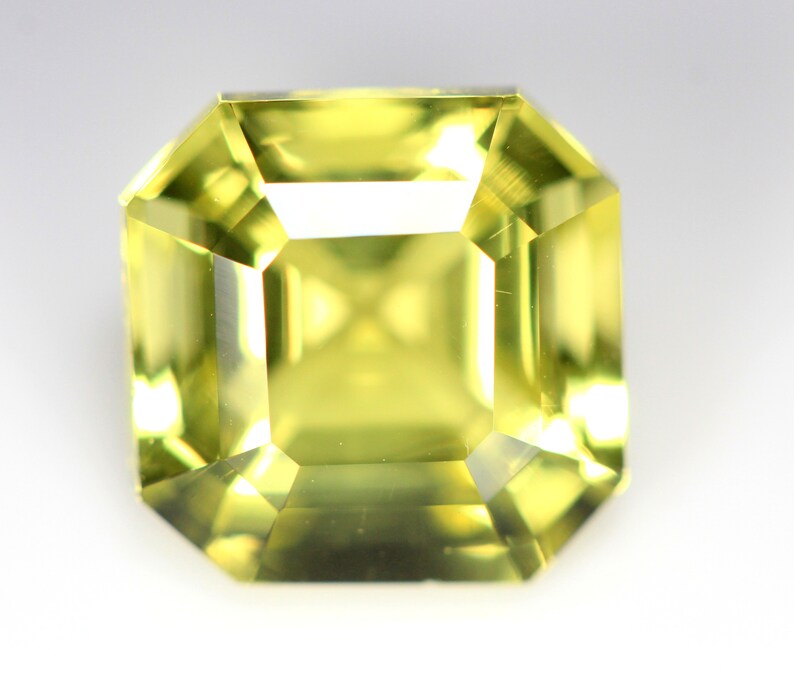 May include: A light yellow gemstone with a square emerald cut. The gemstone is faceted and has a high degree of clarity.