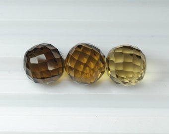 May include: Three faceted gemstone spheres in shades of brown and yellow. The gemstones are arranged in a row against a white background. The spheres have a geometric, multi-faceted design.