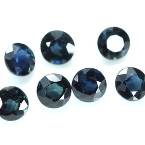 May include: Seven oval-shaped, dark blue gemstones with a faceted cut. The gemstones are arranged in a scattered pattern on a white background.