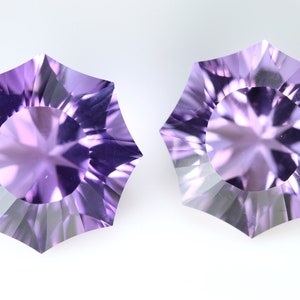 May include: Two faceted, starburst-shaped gemstones with a light purple hue. The gems have a central circular facet surrounded by radiating, triangular facets. The background is plain white, highlighting the gems' intricate cuts and color.
