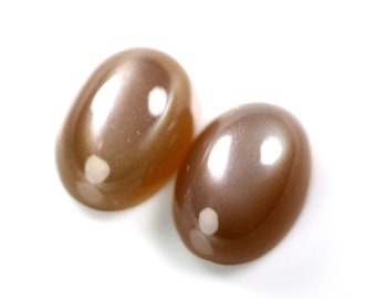 May include: Two oval-shaped, polished gemstones with a warm, brown color and a subtle sheen. The stones are set against a white background, highlighting their smooth, rounded forms. These gemstones are ideal for jewelry making.