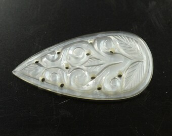 May include: A white pearlescent teardrop-shaped pendant with a carved floral design. The pendant has several small holes drilled through it.