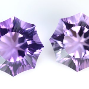 May include: Two faceted, light purple gemstones with a starburst pattern in the center. The gems have a unique, multi-sided shape, and are set against a white background. These gemstones are ideal for jewelry making.