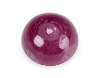 May include: A polished, cabochon-cut ruby gemstone. The deep red gem has a smooth, rounded surface with a high luster, reflecting light. The gemstone is set against a white background.
