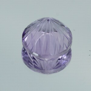 May include: A faceted amethyst gemstone with a purple hue. The gemstone is cut into a round shape with a pointed top.