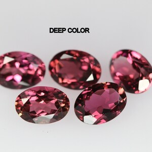 May include: Five oval-shaped gemstones with a deep pink color. The gemstones are arranged in a semi-circle on a white surface. The text "DEEP COLOR" is written above the gemstones.