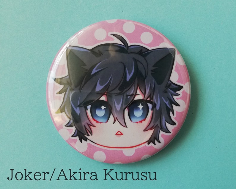 May include: A pink and white polka dot button featuring a cartoon character with black hair, blue eyes, and cat ears. The character's name is "Joker/Akira Kurusu".