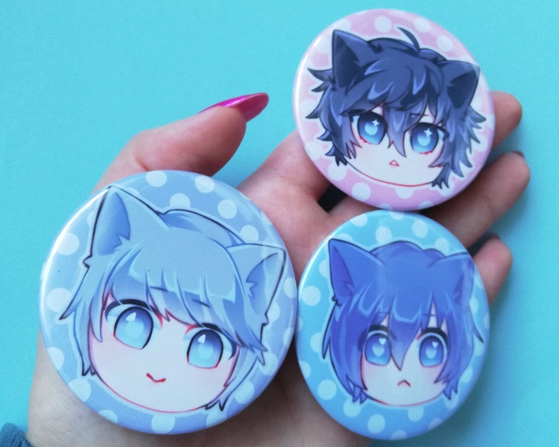 May include: Three round pinback buttons with white polka dot backgrounds. Each button features a cartoon character with blue, purple, or grey hair and cat ears. The characters have large blue eyes and are smiling or frowning.