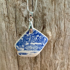 May include: A silver chain necklace with a blue and white porcelain pendant. The pendant is a diamond shape with a floral design.