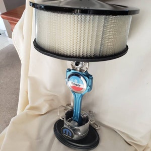 May include: A blue and silver Mopar themed table lamp made from a car engine piston. The lampshade is a black and white air filter.