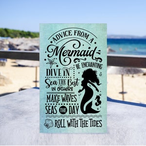 May include: A teal blue sign with a mermaid silhouette and the text "Advice from a Mermaid: Be Enchanting, Dive in Sea the Best in Others, Make Waves Seas the Day, Roll with the Tides".