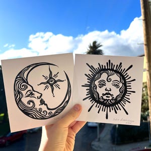 Pode incluir: Duas impress&otilde;es de lin&oacute;leo em preto e branco de uma lua crescente com um rosto e um sol com um rosto. A impress&atilde;o da lua tem uma estrela com um olho no centro. A impress&atilde;o do sol tem o texto "Sofia Lashbrooke 2022".