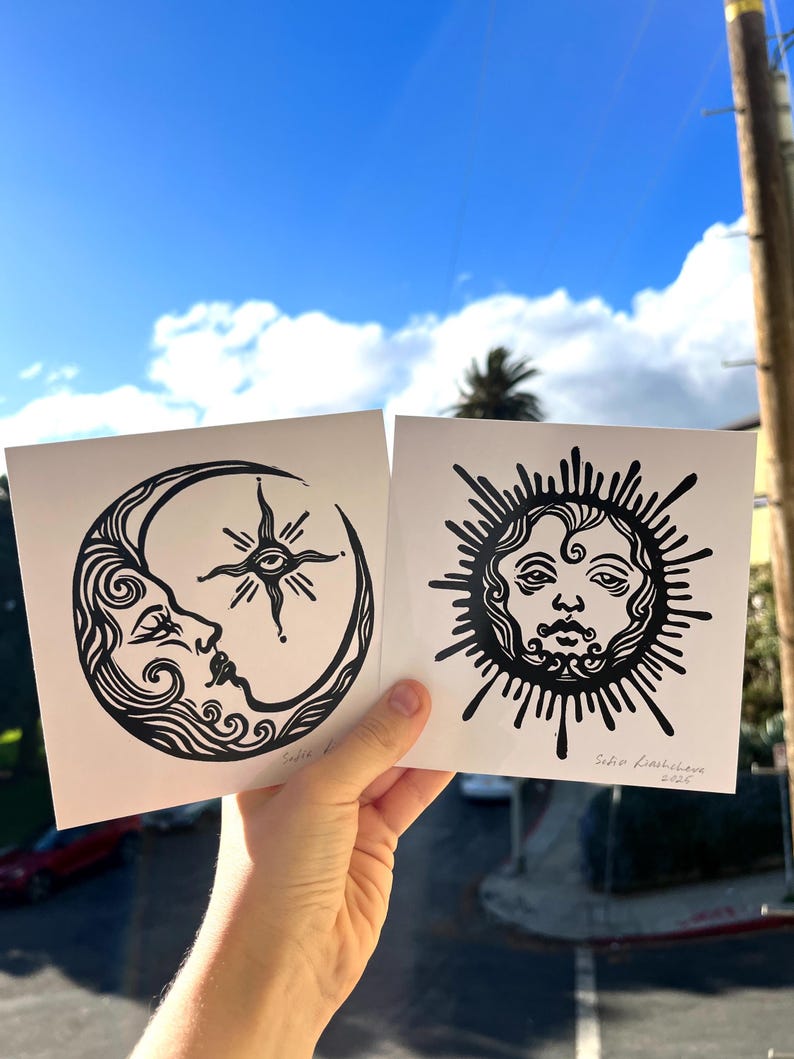 Pode incluir: Duas impress&otilde;es de lin&oacute;leo em preto e branco de uma lua crescente com um rosto e um sol com um rosto. A impress&atilde;o da lua tem uma estrela com um olho no centro. A impress&atilde;o do sol tem o texto "Sofia Lashbrooke 2022".