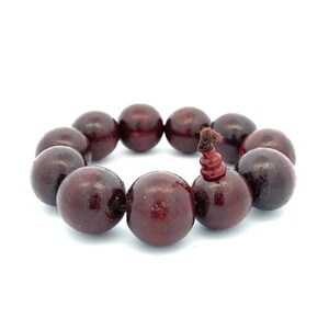May include: A dark red wooden beaded bracelet with a brown string tie.