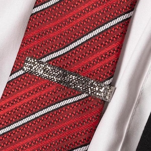 Puede incluir: Una corbata de rayas rojas y blancas con un clip de corbata plateado. El clip de corbata tiene un diseño texturizado.