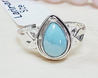 May include: A silver ring with a teardrop-shaped turquoise stone set in a silver bezel. The ring has a textured band with a small silver heart on each side of the stone.